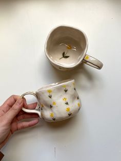 two coffee mugs with yellow flowers on them are being held by someone's hand