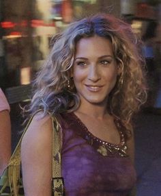 a close up of a person wearing a purple dress and holding a purse on the street