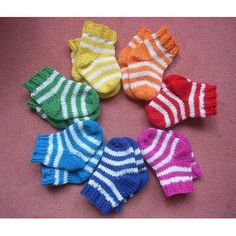 six knitted baby mittens arranged in a circle on a pink surface with white and blue stripes