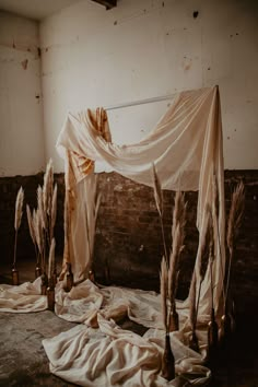 an abandoned room with dried plants and cloth draped over it