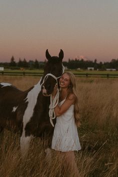 a woman standing next to a brown and white horse on top of a grass covered field