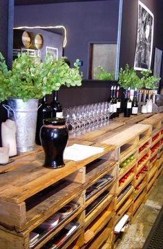 a wooden shelf filled with lots of bottles and glasses next to potted plants on top of a table