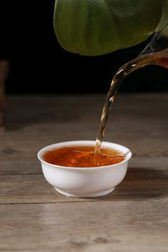 a person pouring sauce into a bowl on top of a wooden table next to a potted plant