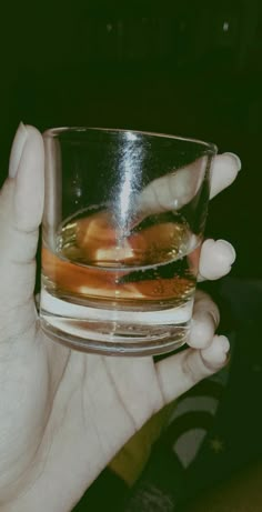 a person holding a glass filled with liquid and ice cubes in their hands,