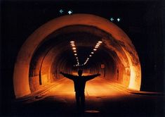 a man standing in the middle of a tunnel with his arms spread out and lights on