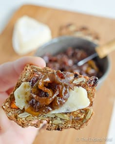 someone is holding up a piece of bread with raisins and cheese on it