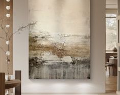 an abstract painting hangs on the wall in a modern living room with white and brown accents