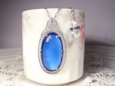 "I am so excited to be offering an exquisite antique Edwardian/Art Deco 1930s era rhodium plated filigree rich sapphire blue glass cabochon pendant necklace. This will be as gorgeous with a pair of jeans and a tee as it will be with a Bridal gown. (The perfect \"Something Old\" and \"Something Blue\".) I can't tell you how much I love this antique treasure! It's designed like a camphor glass necklace of the period but has a an amazing blue cabochon rather than camphor glass center. The pendant f Heirloom Blue Necklaces For Weddings, Vintage Blue Jewelry For Wedding, Vintage Blue Wedding Jewelry, Antique Blue Jewelry For Wedding, Antique Blue Wedding Jewelry, Blue Art Deco Jewelry For Wedding, Blue Filigree Necklace For Wedding, Wedding Something Old, Wedding Something Blue