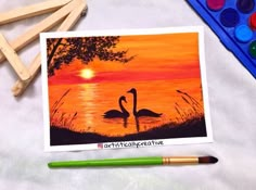 two swans in the water at sunset with paintbrushes and crayons next to them