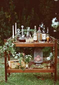 an outdoor bar cart with liquor bottles and candles on the top, surrounded by greenery