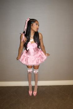 a woman in a pink dress is standing against a wall with her hands on her hips