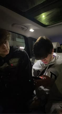 two young men sitting in the back of a car looking at their cell phones