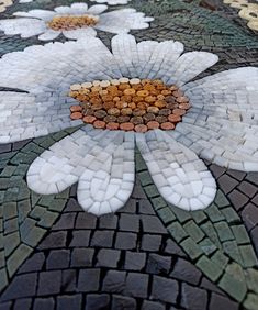 a flower made out of white and brown pebbles on a mosaic tile floor with flowers in the center