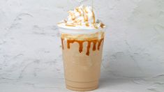 a drink with whipped cream and caramel drizzled on the top is sitting in front of a white wall