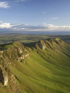 an aerial view of the green hills and valleys in the distance, with blue skies above