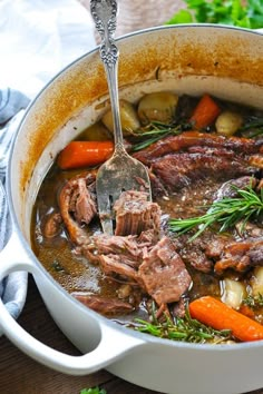 a pot filled with beef and carrots on top of a wooden table next to a spoon