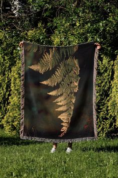 a woman holding up a tapestry with a fern on it in front of some bushes