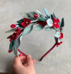 a hand is holding a red flower and green leaf headband