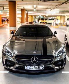 the front end of a silver car in a parking garage with two other cars behind it