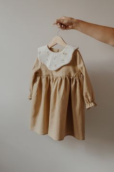 a person holding a baby's dress on a hanger