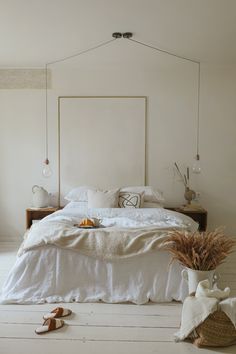 a bed with white linens and pillows in a bedroom next to a plant on the floor