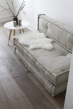 a white couch sitting on top of a wooden floor next to a table with flowers