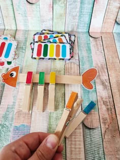 a hand holding wooden pegs with different colored fish on them and some other toys in the background