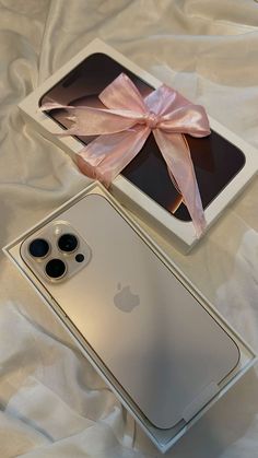 an apple phone with a pink bow next to it on a white bed sheet,