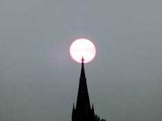 a church steeple with the sun in the sky behind it and a red light on top