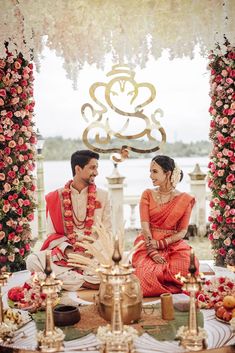 a man and woman sitting in front of a table with flowers on it, posing for the camera