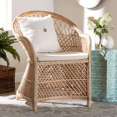 a wicker chair with white pillows on it in front of a vase and potted plant