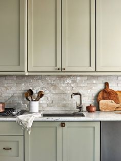 a kitchen with green cabinets and white marble counter tops is pictured in this image, there are wooden utensils on the sink