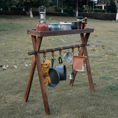 an outdoor pot rack with pots and pans hanging from it's sides in the grass