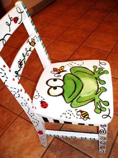 a white wooden chair with a frog painted on it's back and seat cover