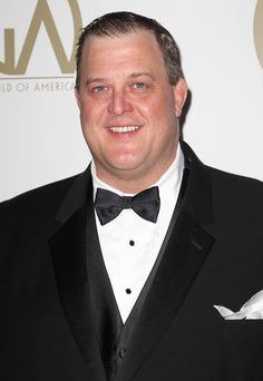 a man in a tuxedo smiles for the camera at an awards event,