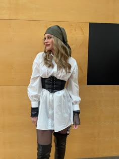 a woman in a white shirt and black skirt standing next to a wooden wall wearing thigh high boots