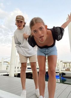 two people standing on a dock with one making a face and the other sticking his tongue out