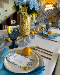 the table is set with blue and yellow flowers, lemons, and gold cutlery