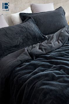 an unmade bed with black sheets and pillows