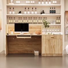 a desk with a computer on top of it in front of shelves filled with bottles