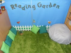 a room with green grass and pillows on the floor next to a blue sign that says reading garden