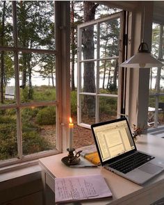 an open laptop computer sitting on top of a desk next to a candle and window