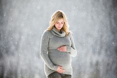 a pregnant woman standing in the snow with her hands on her stomach and looking down