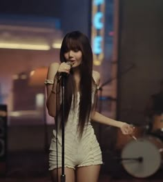 a woman with long hair holding a microphone in front of a mic and standing on stage