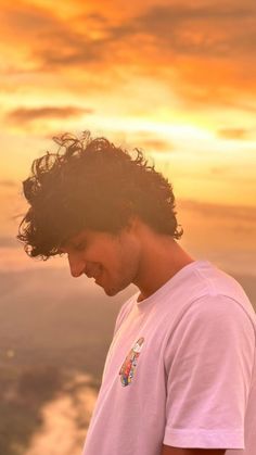 a man standing on top of a mountain looking down at his cell phone while the sun is setting