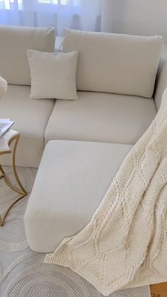 a white couch sitting next to a table with a lamp on top of it and a blanket draped over it