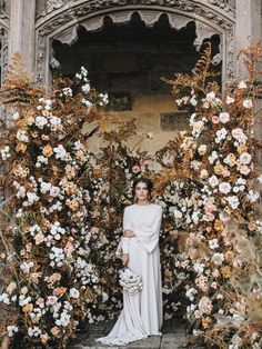 a woman is standing in front of flowers and ivys with her arms raised up