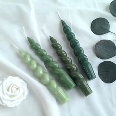 three green candles sitting next to each other on a white sheet with leaves and flowers