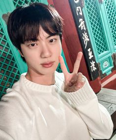 a young man making the peace sign with his hand in front of him and wearing a white sweater