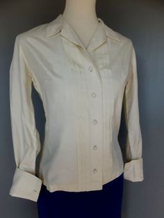 "A classic style blouse that will make a fabulous addition to a professional girl's working wardrobe. Tuxedo style. Condition:  Excellent.    French cuffs.  Off white, ivory in color.  Really good quality fabric.  No fabric label.  Feels like it could be polished cotton or something better.  Feels great. Please keep in mind that all monitors show color differently and that the color may not be exact. Bust:  up to 38\" Waist:  32 Shoulder to shoulder:  15 Sleeve:  21 Length:  23-1/2, measuring fr Classic Daywear Blouse, Classic Fitted Blouse With Button Cuffs, Fitted Classic Blouse With Button Cuffs, Classic Formal Cotton Blouse, Classic Blouse For Daywear, Cream Collared Shirt With Button Cuffs, Classic Beige Shirt For Daywear, Classic Fitted Collar Blouse, Classic Cream Blouse For Work